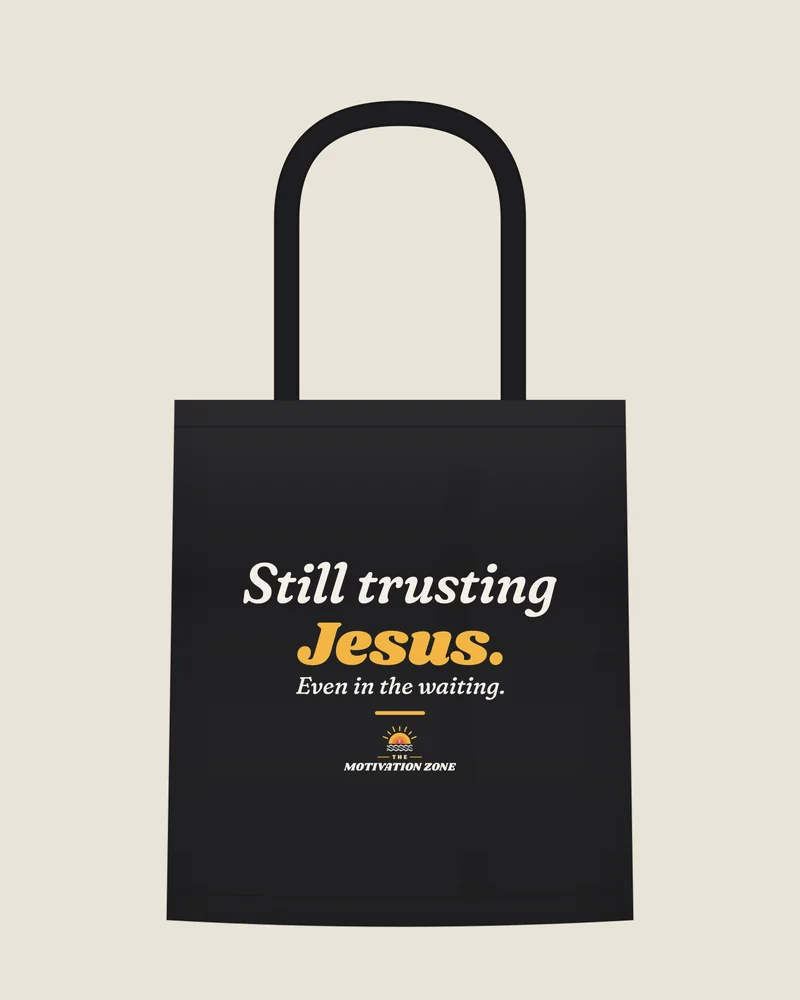 Black tote bag with the print “Still trusting Jesus.”, front view (illustration)